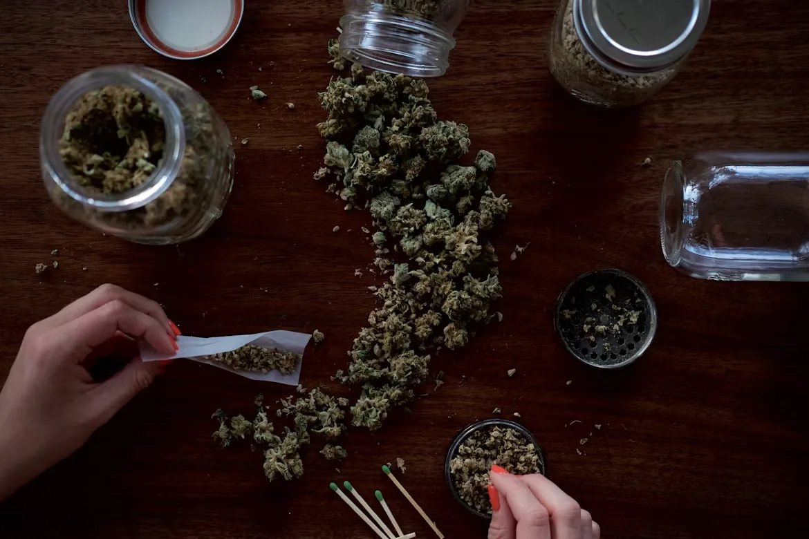 Overhead view of jars, a grinder and rolling papers on a dark timber table