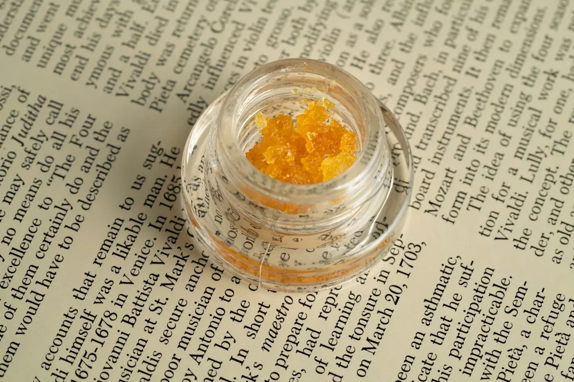A jar of golden cannabis extract resting on an open book