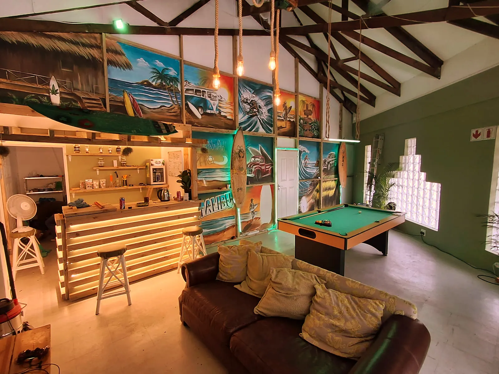 The Die Groen Kamer lounge — timber tiki bar, surf murals, pool table and leather sofa